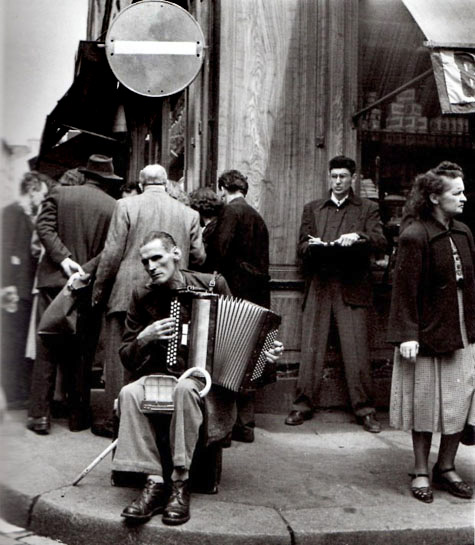 laccordeoniste-rue-mouffetard Paris 1951 by Robert Doisneau - A seated man playing his accordion on a busy corner