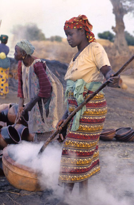 Quenching - Steam rises from a burning hot-pot that-has been immersed in the berry mixture. The older woman-behind is picking up a smaller pot with a pair of tongs