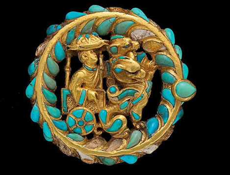 golden-boot-buckle--decorated-with-turquoise-and-carnelian A man rides under a parasol in a cart pulled by a pair of winged felines.