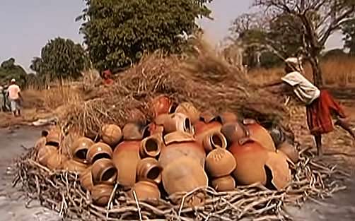 preparing a stack of pottery for firing in Mali