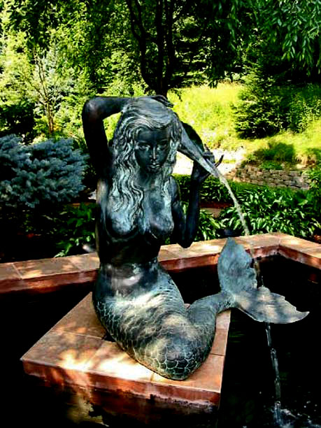 Bronze seated mermaid-fountain in a garden pond