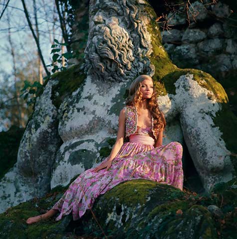 model-veruschka-sitting-on-the-baroque-sculpture-of-a-man-in-the-wearing-pink-floral-gypsy-dress-with-a-sash-at-the-waist-and-a-little-beaded-bolero-by-ken-scott